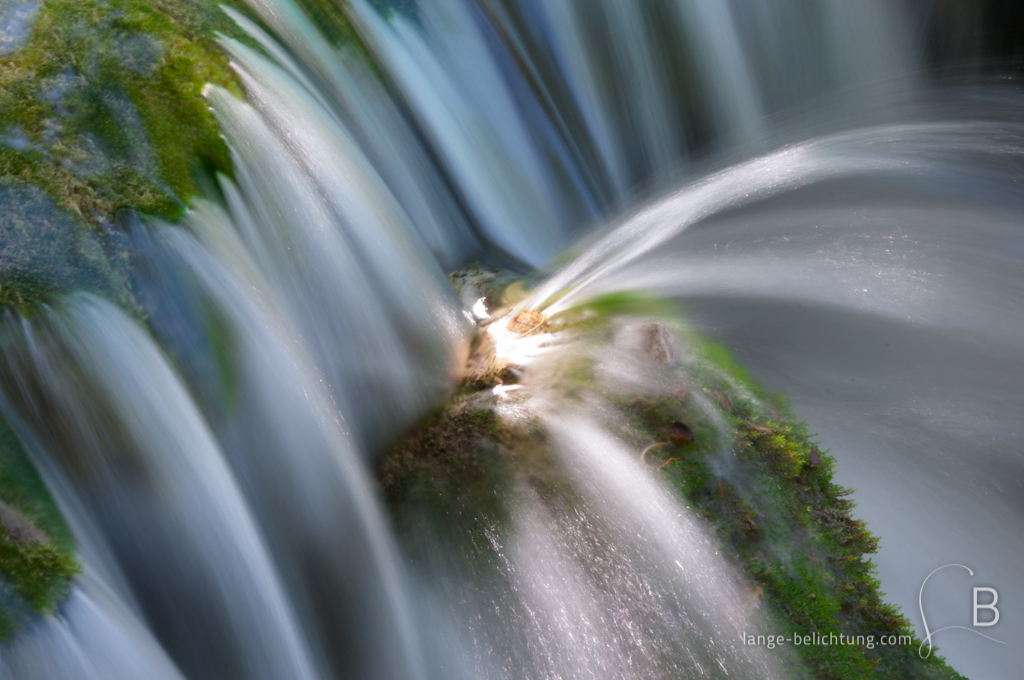 Ein Wasserfall läuft über Moos und wird von einem Felsvorsprung abgelenkt