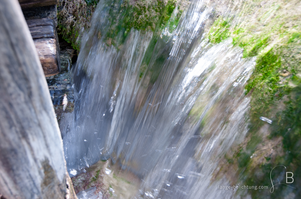 Direkt an einem Holzweg fließt das Wasser über Moos bewachsene Felsen