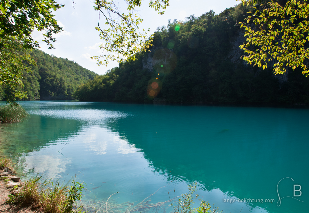 Zwischen den Bergen in Kroatien im Nationalpark Plivicer Seen erstreckt sich ein See zwischen Wäldern. Das Wasser an diesem sonnigen Tag schimmert türkis und reflektiert die Umgebung.