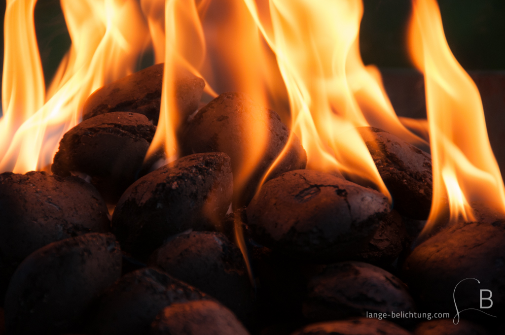 Grillkohle aus Holz wurde mithilfe von Grillanzünder angezündet. Die Kohle ist klar erkennbar ebenso die Flammen, die scheinbar um die Kohle herum lodern.