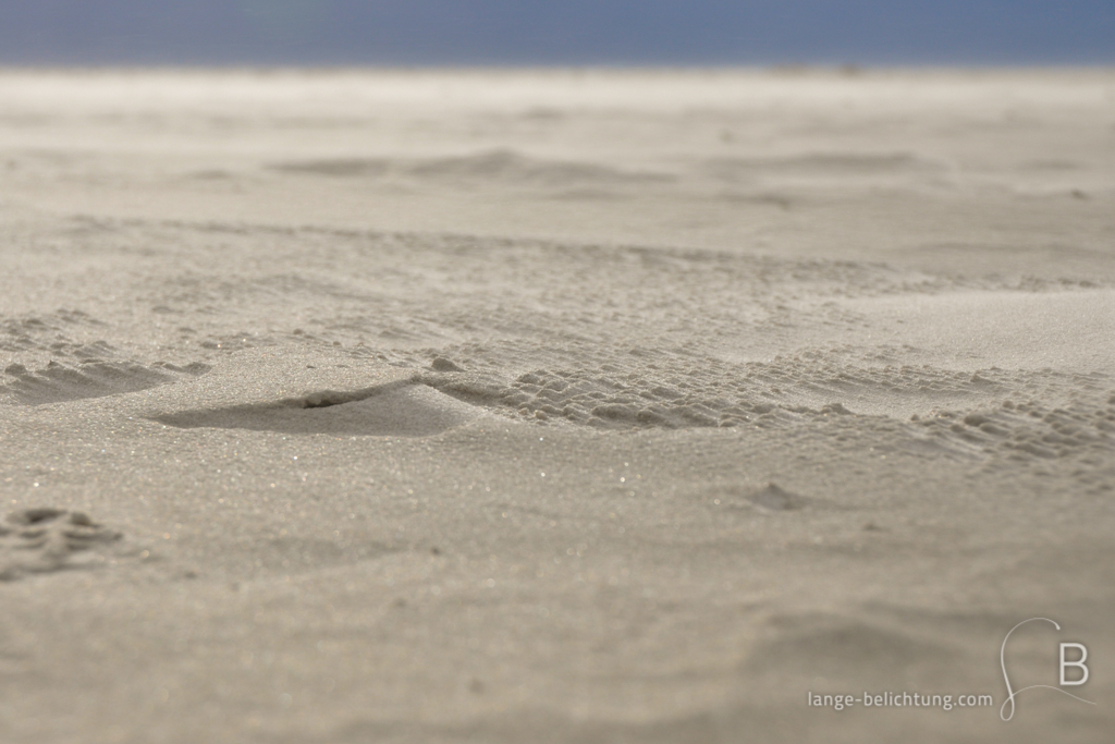 Der Wind hat einmalige Spuren in den Sand gezaubert. Bis zum Horizont sieht man den Strand. Im Vordergrund kleine aufgehäufte typische Sandwellen.