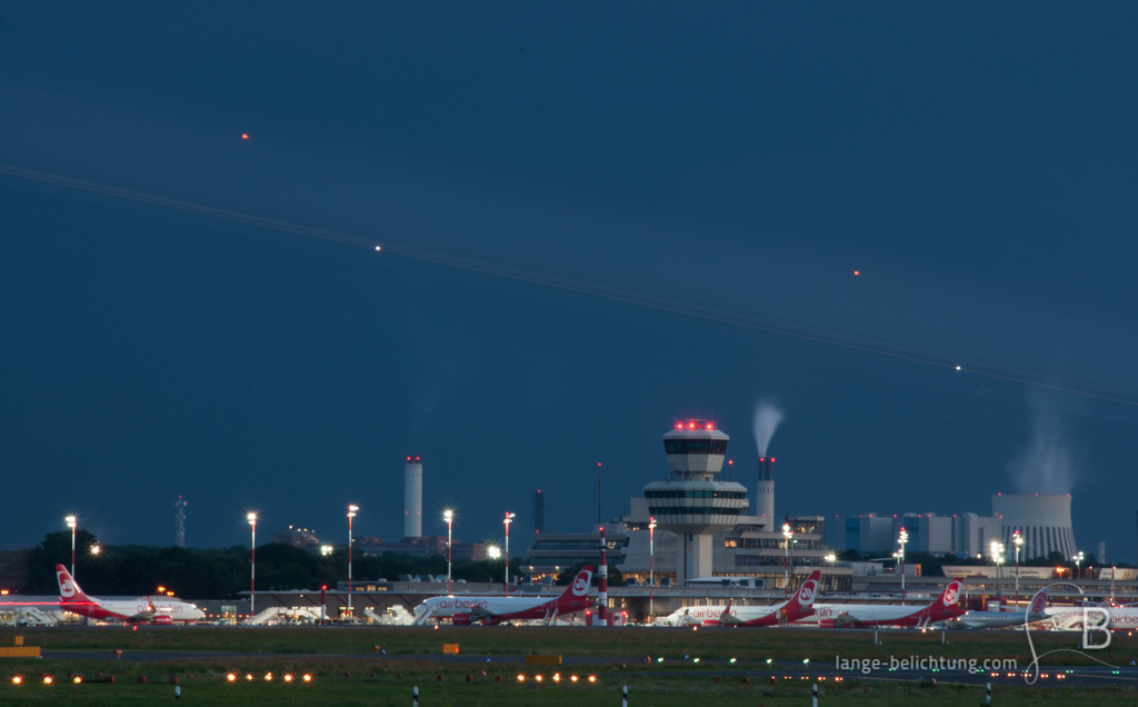 Der Flughafen Tegel bei Nacht. Im Hintergrund erkennt man das Kraftwerk in Spandau. Ein Streifen lässt ein vorbeifliegendes Flugzeug erkennen.